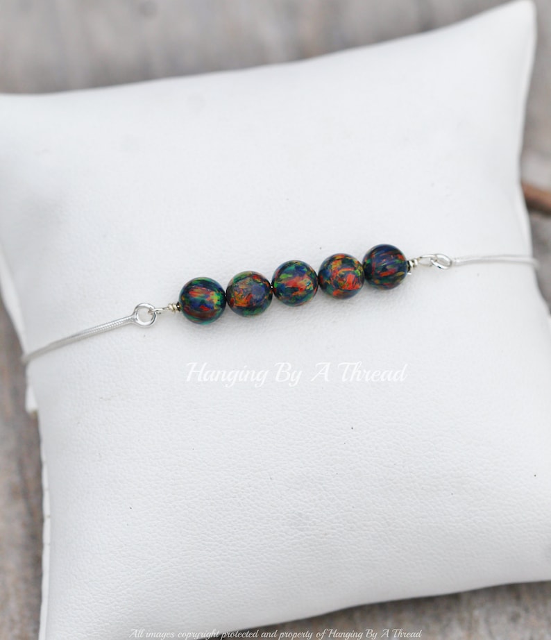 May include: A silver chain bracelet with six iridescent black beads. The beads have a green, orange, and red pattern.