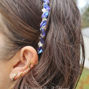 Pu&ograve; includere: Un cerchietto di cristallo blu e argento con un design a forma di lacrima. Il cerchietto &egrave; indossato da una persona con capelli lunghi e castani.