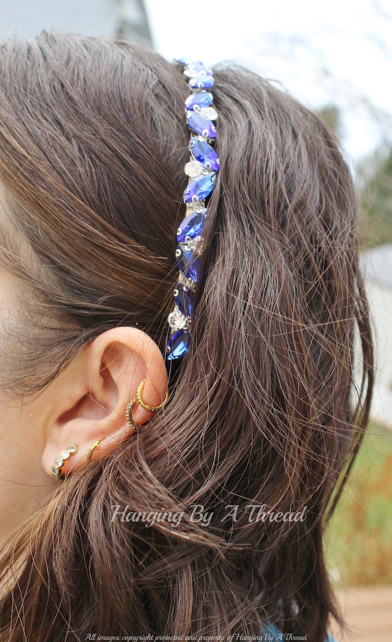 Pu&ograve; includere: Un cerchietto di cristallo blu e argento con un design a forma di lacrima. Il cerchietto &egrave; indossato da una persona con capelli lunghi e castani.