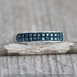 May include: A silver band ring with two rows of small, blue diamonds. The ring is on a wooden surface.