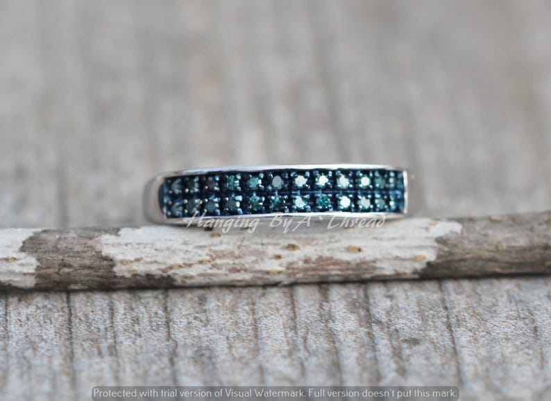 May include: A silver band ring with two rows of small, blue diamonds. The ring is on a wooden surface.
