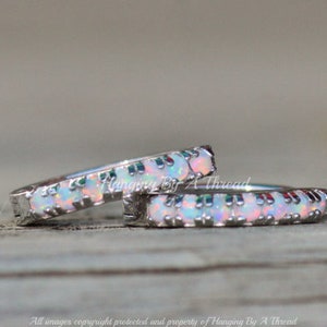 May include: Two silver hoop earrings with a row of white opal stones around the edge. The earrings are on a wooden surface.