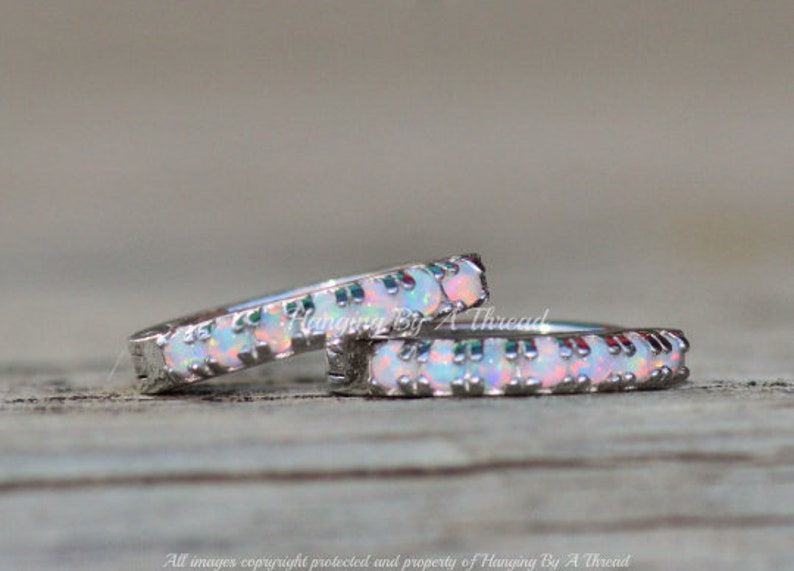 May include: Two silver hoop earrings with a row of white opal stones around the edge. The earrings are on a wooden surface.