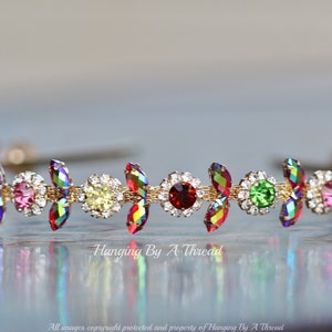May include: A gold headband with a row of colorful rhinestones. The rhinestones are in a variety of shapes and sizes, including round, oval, and marquise. The headband is a delicate and elegant accessory.