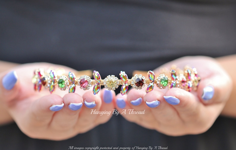 May include: A gold headband with iridescent, multi-colored gemstones. The headband is decorated with small, clear rhinestones.