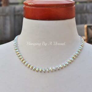 May include: A delicate necklace with iridescent, marquise-shaped crystals. The crystals are set in a row, creating a sparkling choker style. The text "Hanging By A Thread" is visible on the image.