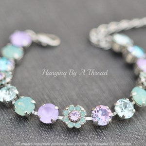 May include: A silver bracelet with a chain link design features alternating pastel blue, lavender, and light purple crystal beads. The bracelet has a lobster claw clasp.