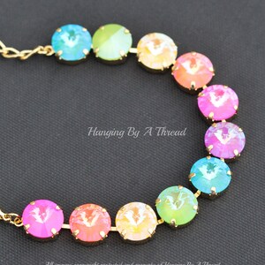 May include: A rainbow-colored crystal necklace with gold chain links. The crystals are round and have a faceted design. The necklace is arranged in a rainbow pattern, with each crystal a different color.
