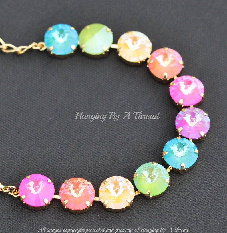 May include: A rainbow-colored crystal necklace with gold chain links. The crystals are round and have a faceted design. The necklace is arranged in a rainbow pattern, with each crystal a different color.