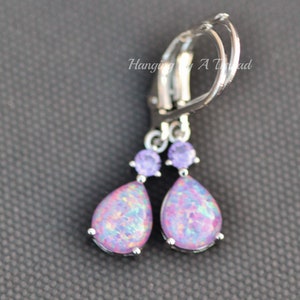 May include: Silver teardrop earrings with a purple opal stone and a smaller purple crystal accent.  The earrings have a lever back closure.