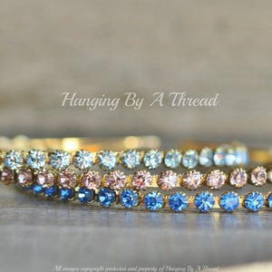May include: Three gold hoops with a graduated ombre design of light blue, pink, and dark blue rhinestones.  The hoops are stacked on top of each other.