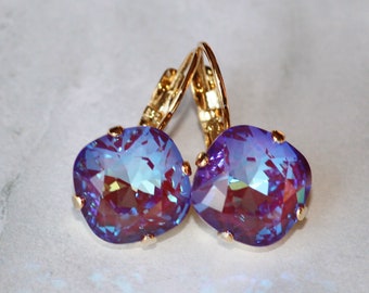 Puede incluir: Un par de pendientes de oro con piedras de cristal púrpura iridiscentes. Las piedras son facetadas y tienen un acabado brillante.