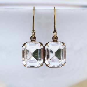 May include: A pair of vintage-style earrings featuring clear, rectangular crystals set in antique gold-tone metal. The crystals have a faceted cut, reflecting light. The earrings have a simple hook closure.