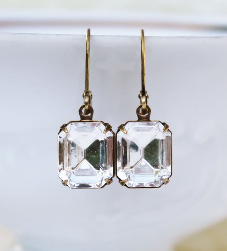 May include: A pair of vintage-style earrings featuring clear, rectangular crystals set in antique gold-tone metal. The crystals have a faceted cut, reflecting light. The earrings have a simple hook closure.