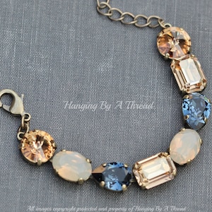 May include: A vintage-style bracelet featuring a variety of colorful gemstones in shades of amber, blue, and opalescent white. The bracelet has an antique brass finish and a lobster clasp closure. The text "Hanging By A Thread" is visible.