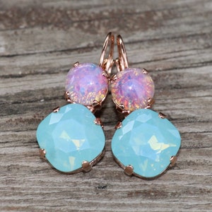 May include: A pair of rose gold earrings featuring two light blue, square-cut stones and two round, pink stones. The earrings are set against a wooden background.