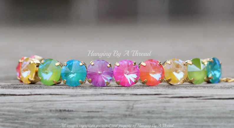 May include: A rainbow-colored crystal bracelet with gold accents. The bracelet features round, faceted crystals in shades of yellow, green, blue, pink, and orange.
