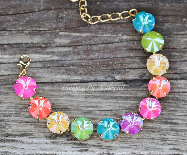 May include: A rainbow crystal bracelet with gold chain and clasp. The bracelet features round, faceted crystals in shades of pink, orange, yellow, green, blue, and purple.
