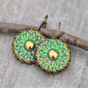 May include: A pair of green and gold earrings with a floral design. The earrings are made of metal and have a hook closure.