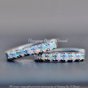 May include: Two silver rings with a row of white opal stones set in each band. The rings are stacked on top of each other.