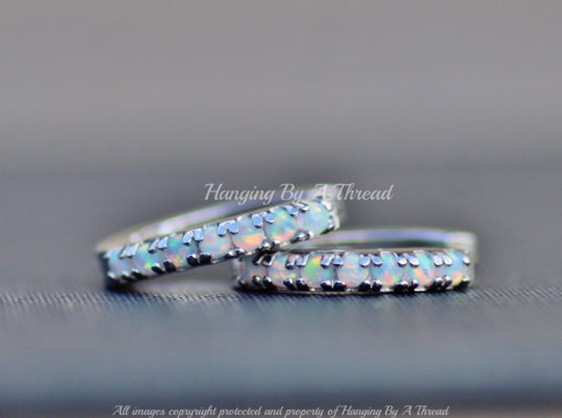 May include: Two silver rings with a row of white opal stones set in each band. The rings are stacked on top of each other.