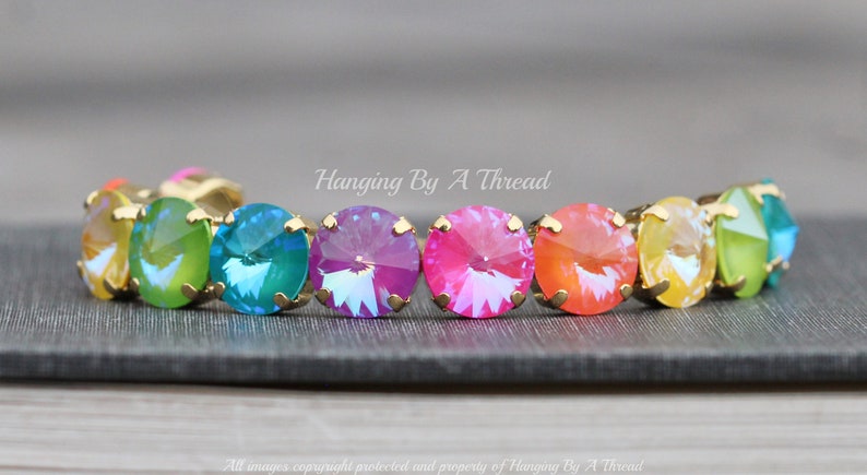 May include: A rainbow-colored crystal bracelet with gold settings. The bracelet features a row of round, faceted crystals in shades of yellow, green, blue, purple, pink, and orange.