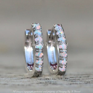 May include: A pair of silver hoop earrings with a row of white opal stones around the hoop.