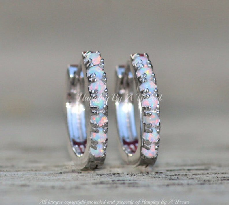 May include: A pair of silver hoop earrings with a row of white opal stones around the hoop.