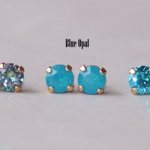 May include: Three pairs of gold stud earrings with different coloured gemstones. The first pair has a green and blue iridescent gemstone, the second pair has a light blue opal gemstone, and the third pair has a teal gemstone.