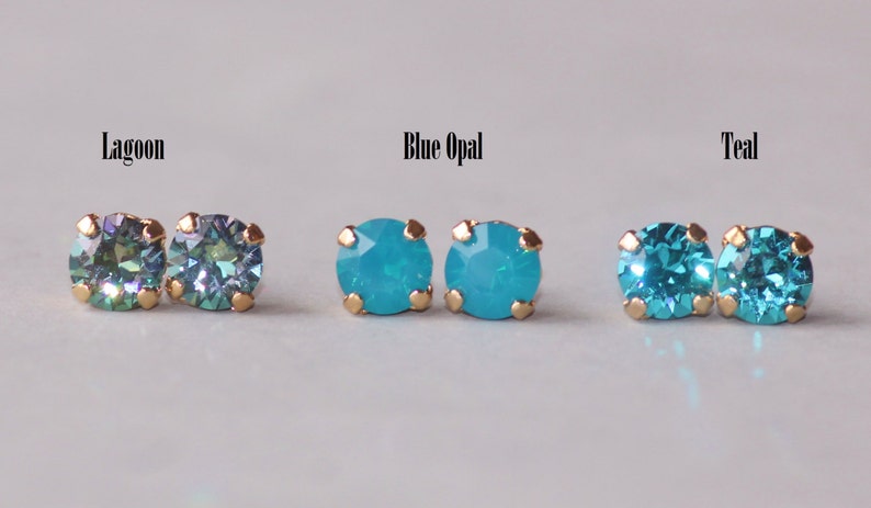 May include: Three pairs of gold stud earrings with different coloured gemstones. The first pair has a green and blue iridescent gemstone, the second pair has a light blue opal gemstone, and the third pair has a teal gemstone.
