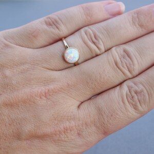 May include: A gold ring with a white opal gemstone. The ring is on a person's finger.