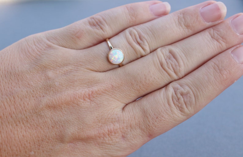 May include: A gold ring with a white opal gemstone. The ring is on a person's finger.