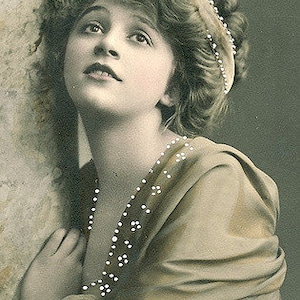 May include: A crocheted blanket with a chevron pattern in shades of white, purple, and blue is hanging on a white brick wall.