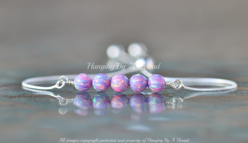 Puede incluir: Un brazalete de cadena de plata con cinco cuentas de color p&uacute;rpura iridiscente. El brazalete es ajustable con un nudo deslizante.