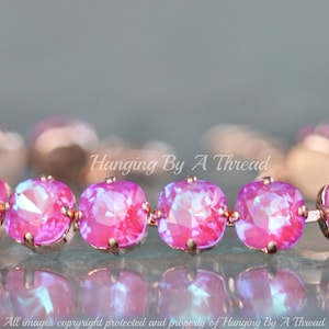 Può includere: Un braccialetto in oro rosa con cristalli rosa iridescenti. Il braccialetto è realizzato con piccoli cristalli quadrati collegati da una sottile catena di metallo. I cristalli sono disposti in un cerchio attorno al polso.