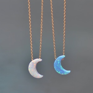 Op de afbeelding: Twee gouden kettingen met halve maan opal hangers. De ene hanger is van witte opaal en de andere van blauwe opaal.