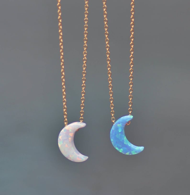 Op de afbeelding: Twee gouden kettingen met halve maan opal hangers. De ene hanger is van witte opaal en de andere van blauwe opaal.