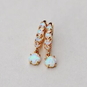 Puede incluir: Aretes de aro de oro con una piedra de &oacute;palo colgante. Los aros est&aacute;n hechos de un alambre delicado y est&aacute;n adornados con peque&ntilde;as piedras de &oacute;palo.