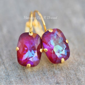 May include: A pair of gold hoop earrings with a rectangular iridescent purple gemstone. The earrings are hanging from a gold hook.