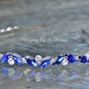 Pu&ograve; includere: Un cerchietto argentato con una fila di strass blu a forma di marquise e strass trasparenti.