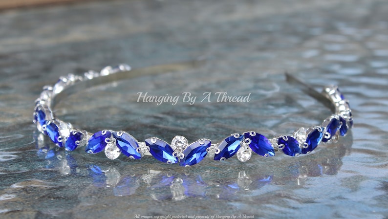 Pu&ograve; includere: Un cerchietto argentato con una fila di strass blu a forma di marquise e strass trasparenti.