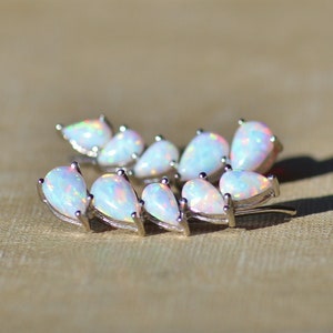 Pu&ograve; includere: Un orecchino ear climber argentato con una serie di opali iridescenti a forma di pera. Gli opali hanno una base bianca lattea con lampi di colore. L'orecchino &egrave; curvo verso l'alto, progettato per essere indossato lungo l'orecchio.