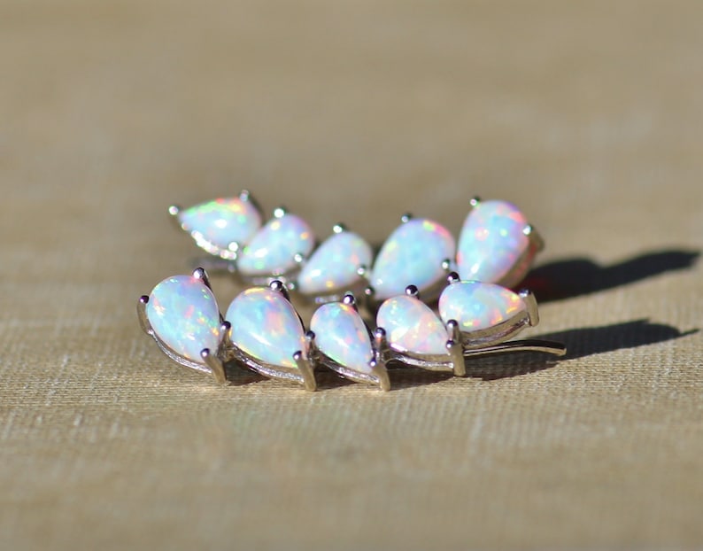 Pu&ograve; includere: Un orecchino ear climber argentato con una serie di opali iridescenti a forma di pera. Gli opali hanno una base bianca lattea con lampi di colore. L'orecchino &egrave; curvo verso l'alto, progettato per essere indossato lungo l'orecchio.
