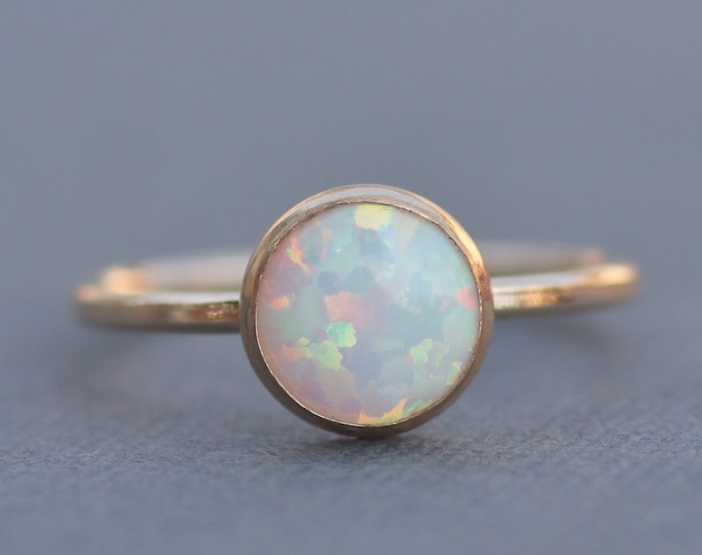 May include: A delicate gold ring with a round, white opal gemstone.