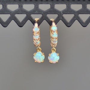 Puede incluir: Aretes de aro de oro con una piedra preciosa de &oacute;palo colgante. Los aros est&aacute;n engastados con peque&ntilde;os &oacute;palos.
