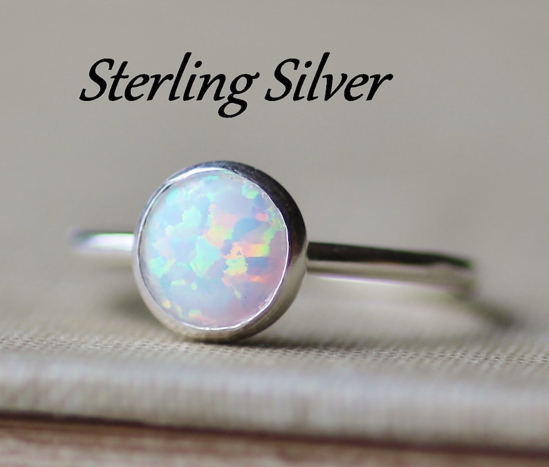 May include: A sterling silver ring with a white opal gemstone. The ring is simple and elegant, with a smooth band and a round opal.