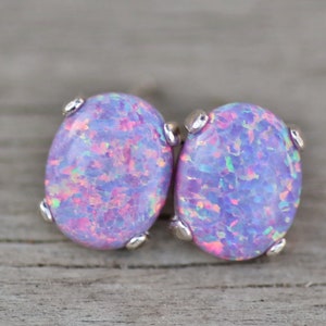 May include: A pair of silver stud earrings with oval-shaped iridescent opal stones. The opals have a light purple base with pink and blue flashes.