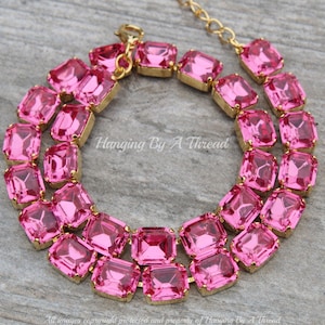 Puede incluir: Un collar de declaración de cristal rosa con detalles de metal dorado. El collar presenta una doble fila de cristales de forma cuadrada.