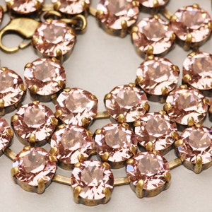 May include: A close-up of a delicate necklace made of small, round, pale pink crystals set in gold-toned metal. The necklace is made of multiple strands of crystals, creating a layered effect.
