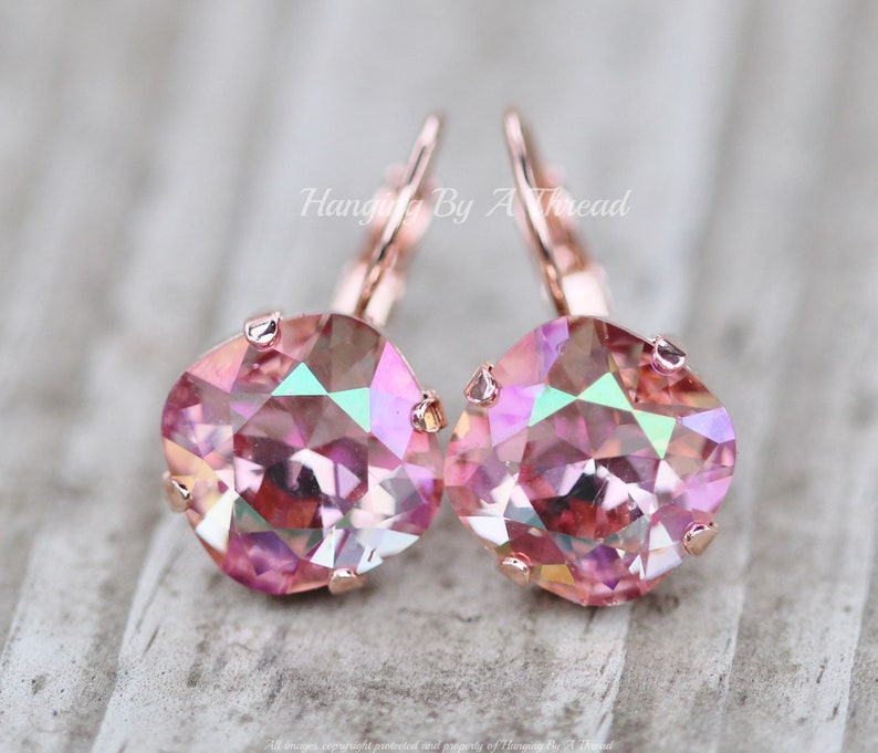 May include: Rose gold earrings with pink iridescent crystal stones. The earrings have a lever back closure.